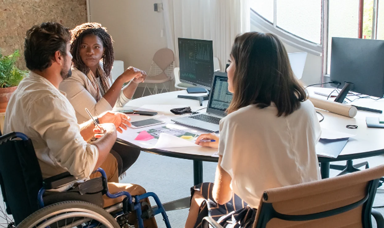 Trois personnes en réunion de travail collaborative, dont une personne en fauteuil roulant